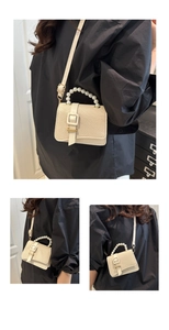 Detail of cream woven mini bag with pearl handle and crossbody strap on black top