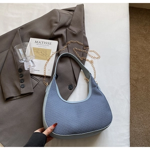 Détail d'un sac demi-lune bleu clair tressé avec chaîne dorée sur un blazer