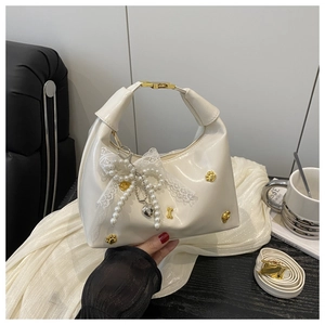Detail of cream hobo bag with gold cat paw studs and pearl lace bow charm accent