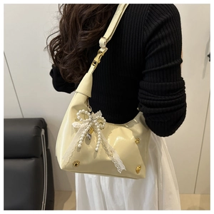 Detail of cream crescent crossbody bag featuring pearl bow and gold cat paw studs