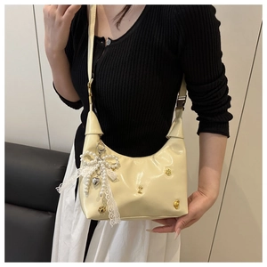 Detail of cream hobo bag with pearl lace bow and golden bone charms on a shoulder