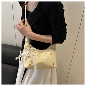 Detail of cream patent leather bag with gold studs and large pearl bow lace pendant