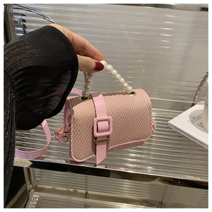 Detailed view of pink woven crossbody bag featuring a large white pearl handle and gold clasp