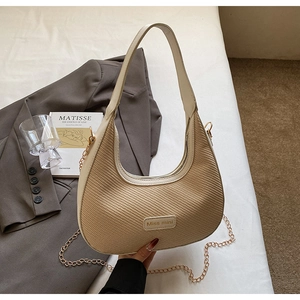 Détail de sac hobo beige en demi-lune avec panneau tissé et chaîne dorée chic