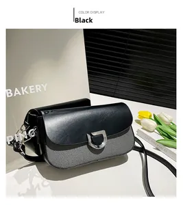 Close-up of black leather crossbody bag with silver D-buckle and decorative charm