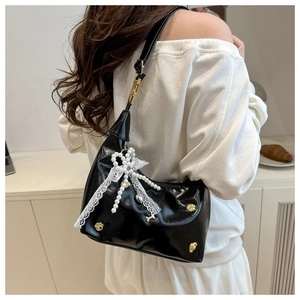 Detail of black glossy hobo bag with pearl bow and white lace pendant decoration