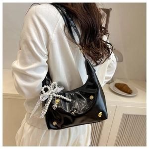 Detail of black glossy shoulder bag with pearl, lace bow, and cat claw metal charms