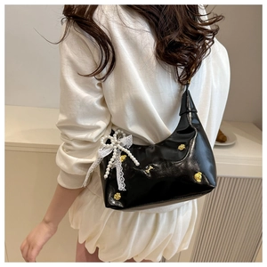 Detail of black patent leather Hobo bag with metal studs and pearl lace bow charm