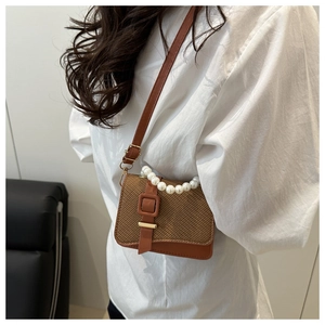 Brown woven crossbody bag with pearl handle and leather strap on white shirt