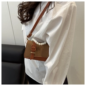 Brown woven crossbody bag with pearl handle and golden buckle worn by a model