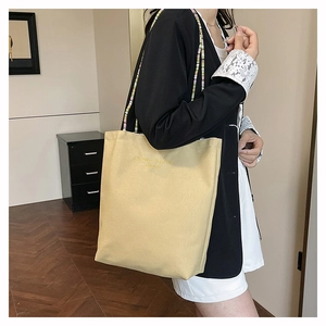Detail of light yellow canvas tote bag featuring Blooming Fashion embroidery and beaded strap