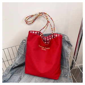 Detail of red tote bag featuring colorful woven handle and checkered lining over denim