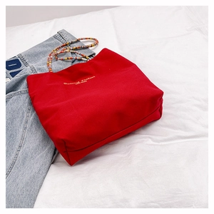 Detail of red canvas tote bag featuring colorful beaded handles and golden fashion lettering