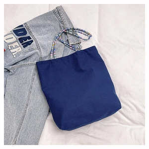 Detail of navy canvas tote bag with colorful beaded shoulder straps on denim background