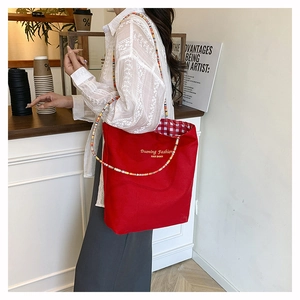 Detailed view of red canvas tote bag with beaded strap and red checkered lining