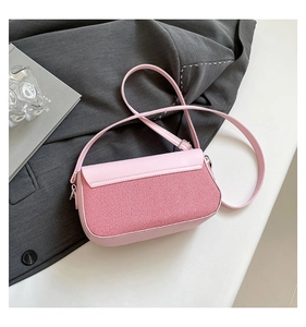 Detail of pink leather crossbody bag with striped fabric back panel on styled desk