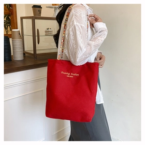 Close-up of red canvas tote bag featuring yellow embroidery and colorful beaded shoulder strap