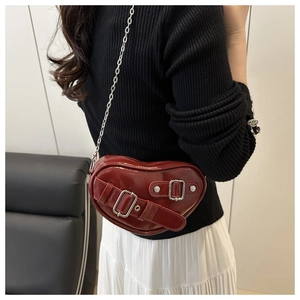 Détail du sac à bandoulière rouge en forme de cœur avec boucles argentées et chaîne