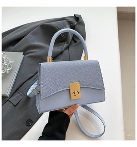 Detail of light blue crossbody bag featuring woven texture flap and gold square lock