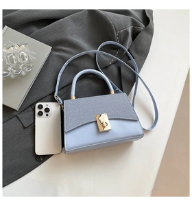 Detail of light blue crossbody bag featuring gold twist lock and a textured flap design