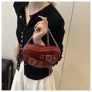 Detail of red heart-shaped shoulder bag featuring glossy finish and silver buckle straps