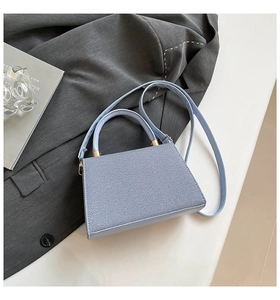 Detail of lilac blue twill fabric texture and gold hardware on a minimalist handbag