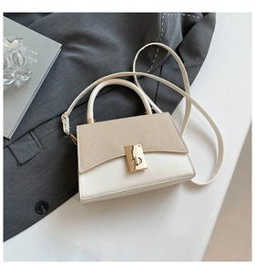 Detail of contrast color crossbody bag with gold twist lock on a minimalist desk setup