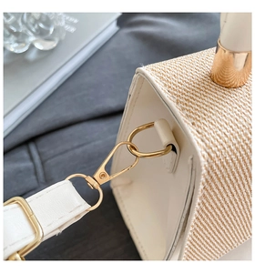 Detail of gold metal hardware and cream leather strap on straw weave handbag