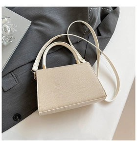 Detail showing woven texture and gold hardware of the cream-colored square crossbody bag