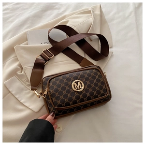 Close-up of vintage pattern crossbody bag with gold M logo on a beige blazer background