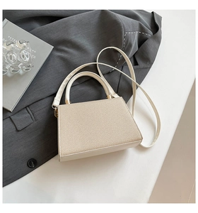 Detail of cream woven texture and smooth leather on a trapezoid crossbody bag