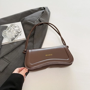 Dark brown leather baguette bag with wavy base design and gold lettering on grey blazer