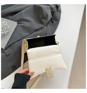 Detailed view of white curved leather handbag featuring golden metal buckle and black lining