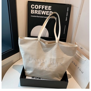 Close-up of off-white canvas tote bag with white 3D letter embroidery and long straps