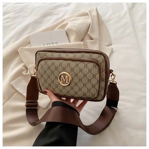 Close-up of vintage monogram crossbody bag with gold M logo and wide fabric strap