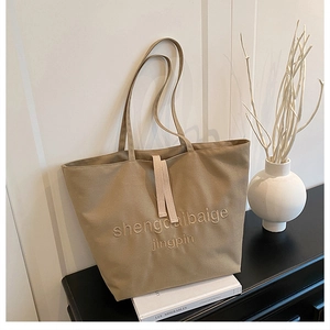 Close-up of khaki canvas tote bag featuring textured lettering and decorative ribbon detail