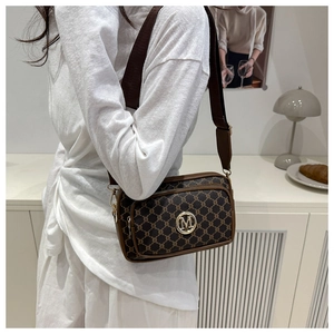 Detailed view of brown letter print crossbody bag with gold M logo and wide strap