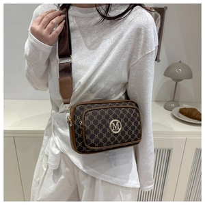 Close-up of brown monogram crossbody bag with metallic M logo and wide fabric strap