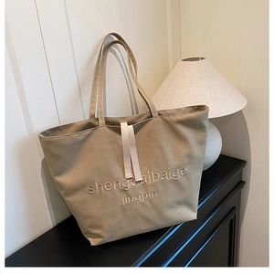 Detail view of khaki canvas tote bag with embroidered letters and decorative ribbon straps