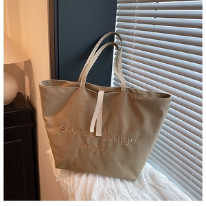 Detail of khaki canvas tote bag featuring premium letter embroidery on white fabric
