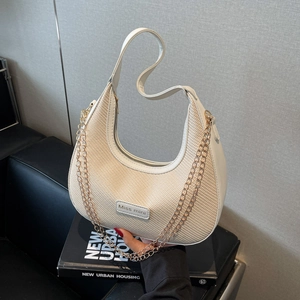 Sac hobo tissé beige avec bordure en cuir et chaîne dorée dans un décor urbain chic