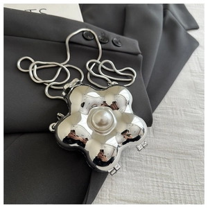 Close-up of flower shaped silver acrylic clutch with large pearl and chain on grey fabric