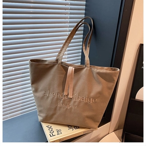 Detail of khaki canvas tote bag with embroidered letters and decorative ribbon straps