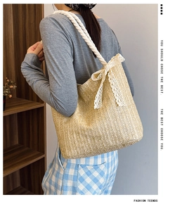 Close-up of woven straw tote bag featuring white rope straps and a delicate lace bow