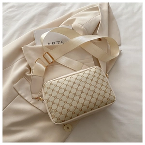 Close-up of beige crossbody bag with vintage monogram pattern and wide nylon shoulder strap