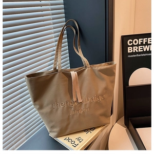 Detail of khaki canvas tote bag featuring embroidered text and decorative drawstrings