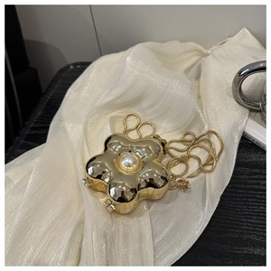 Detail of golden metal flower evening bag with central pearl and snake chain on satin