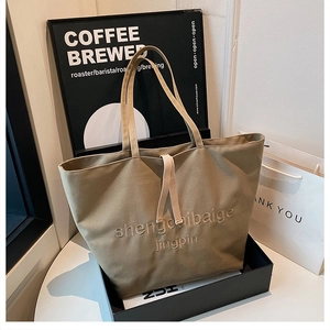 Detailed close-up of large khaki canvas tote bag with embossed lettering on body