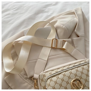 Detail of vintage patterned cream crossbody bag with golden M logo and wide strap