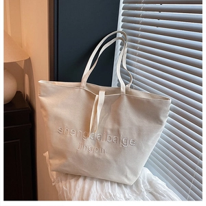Detailed macro view of cream canvas tote bag featuring premium letter embroidery